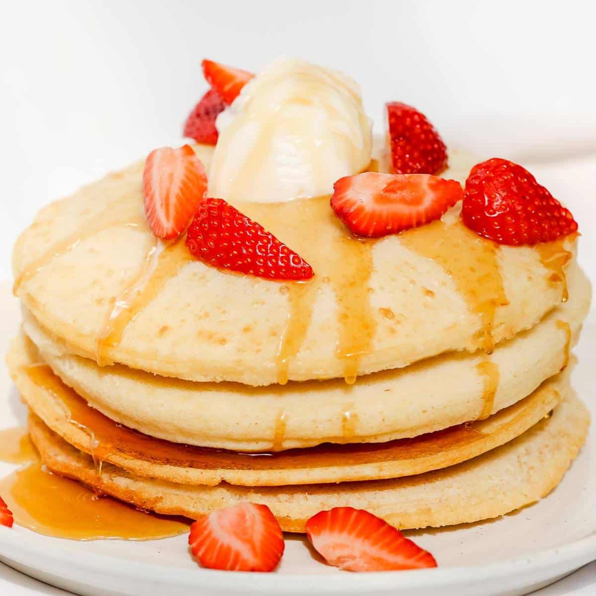 A stack of air fryer pancakes drizzled with maple syrup and topped with ice cream and strawberries.