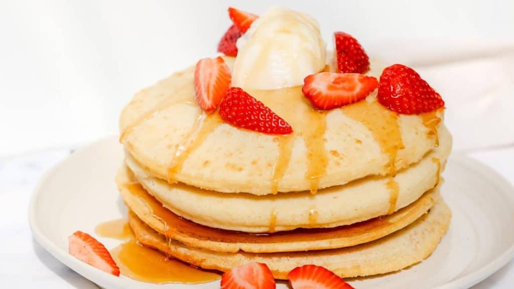 Air fryer pancakes stacked on a white plate topped with ice cream and strawberries.