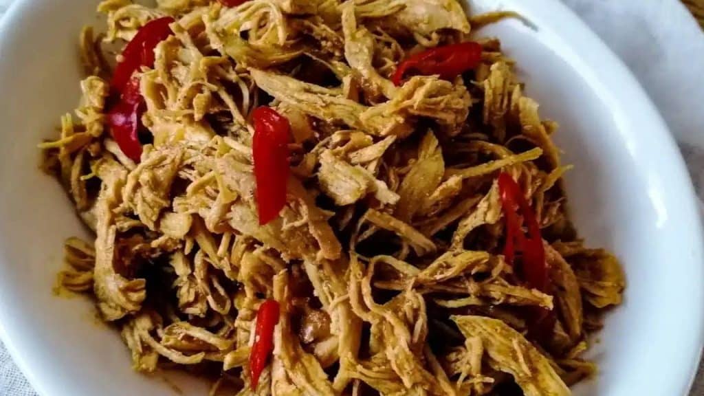 Balinese shredded chicken with red chili slices in an oval white dish.