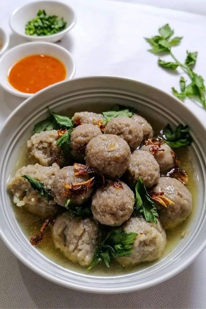 A bowl of Bakso with a small bowl of chili sauce and celery.