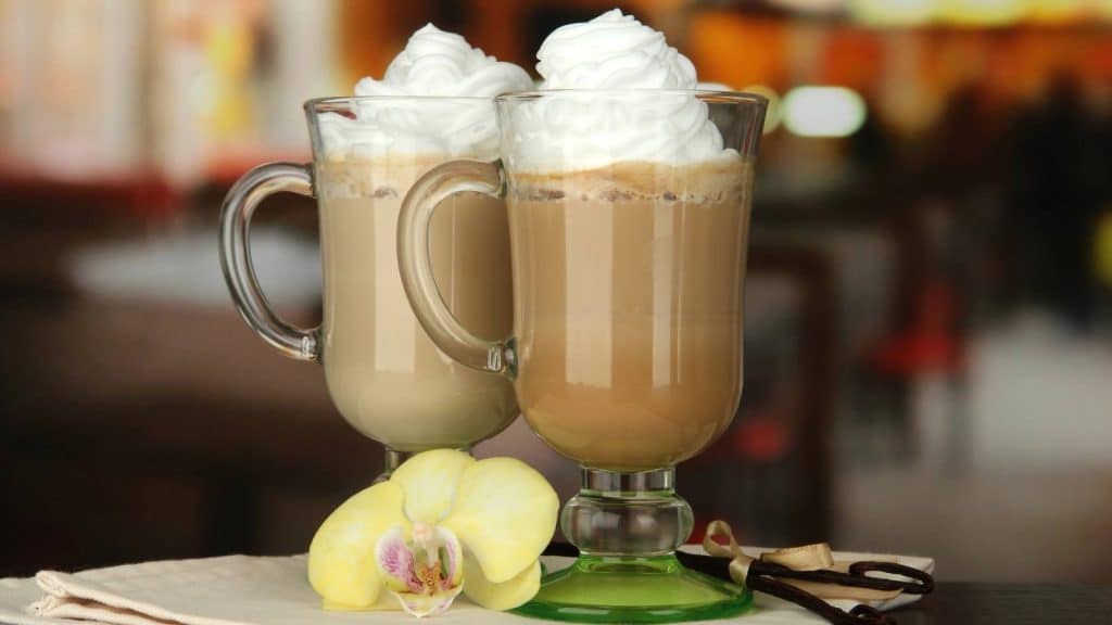 Two glasses of cafe latte topped with whipped cream and an orchid.