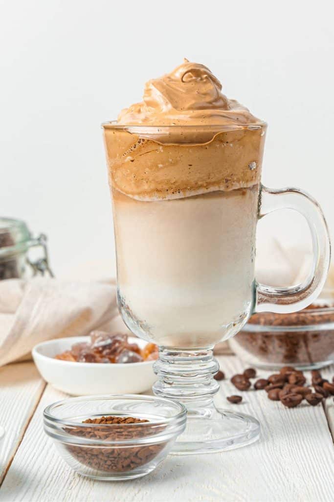 A small bowl of instant coffee with a tall glass of Dalgona coffee.
