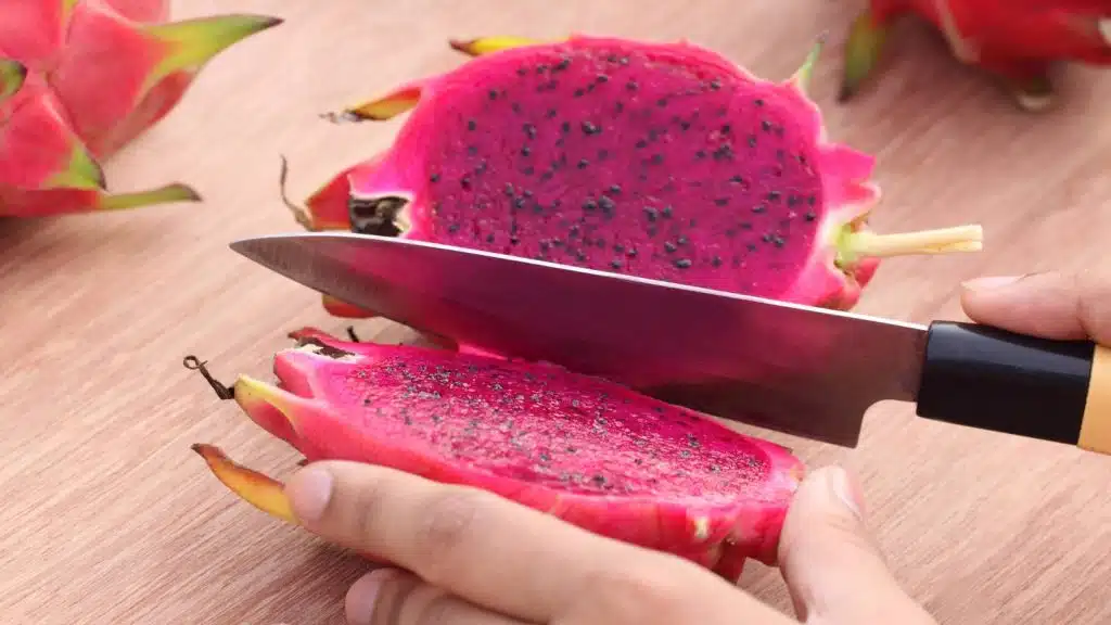 Hands holding a knife and cutting a dragon fruit.