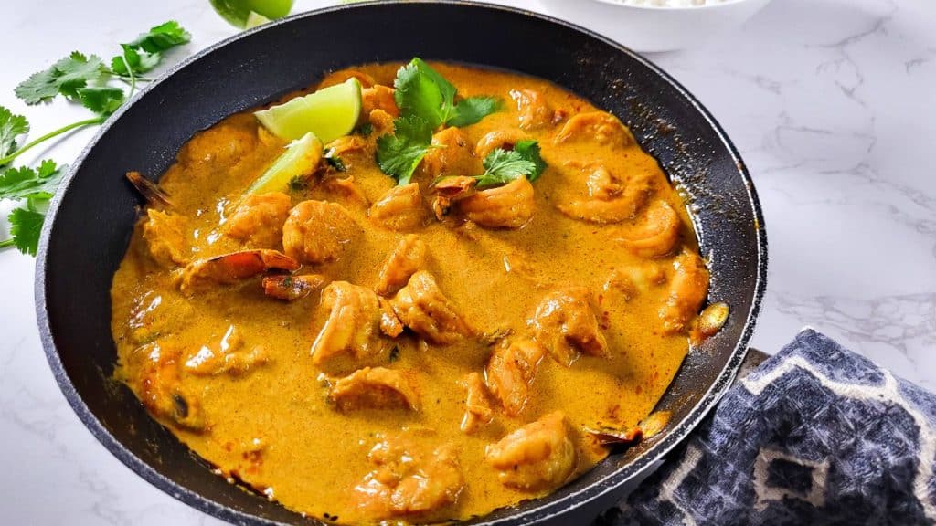 Shrimp curry in a pan garnished with lemon wedges and cilantro.