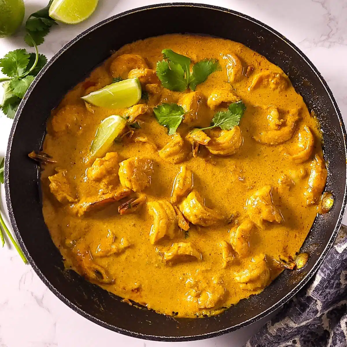 Shrimp Curry in a skillet with lemon wedges and cilantro.