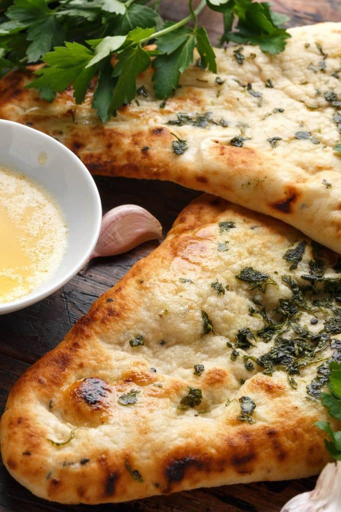 naan breads with parsley and a bowl of melted butter.