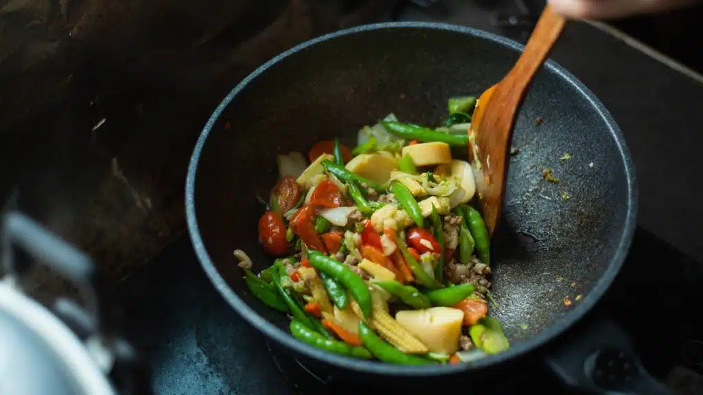 Stir frying vegetables in a wok with a wooden spoon. 