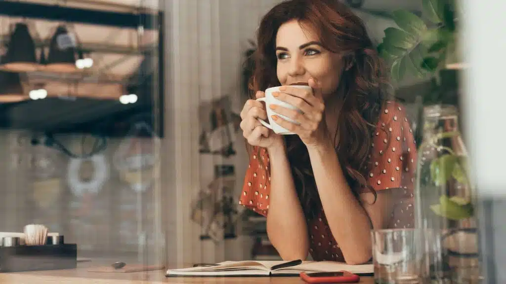A young woman drinking a cup of coffee at a table.