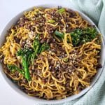 Ground beef noodle stir fry in a white bowl with mint green napkin in the background.