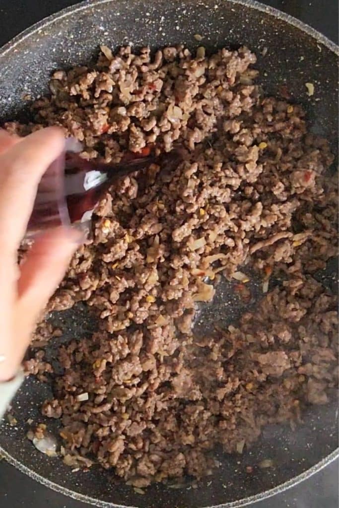 A hand adding soy sauce to spiced ground beef.