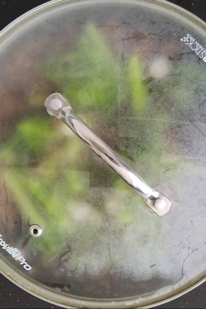 Cooking broccoli in a frying pan with the lid on.