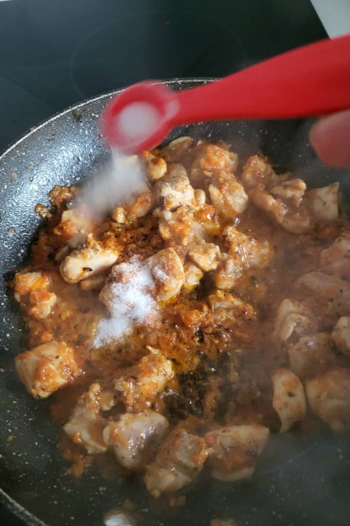 Adding salt to chicken in sun dried tomato sauce.