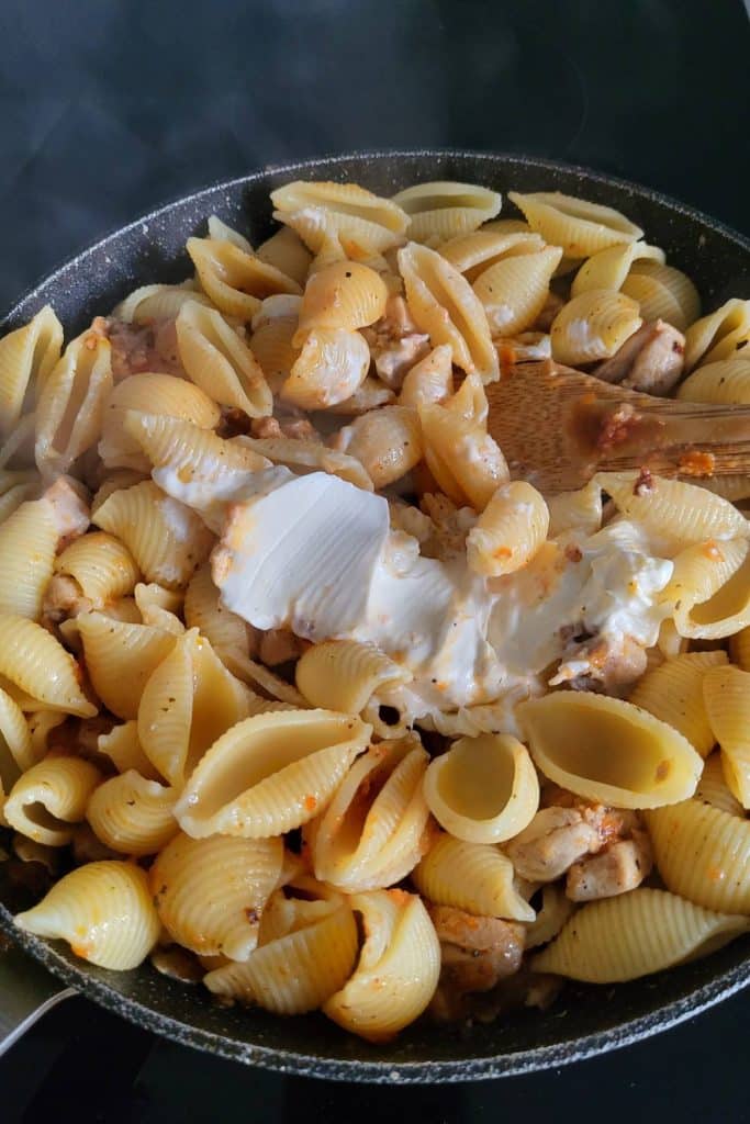 Cooked pasta shells with tomato sauce and cream cheese.