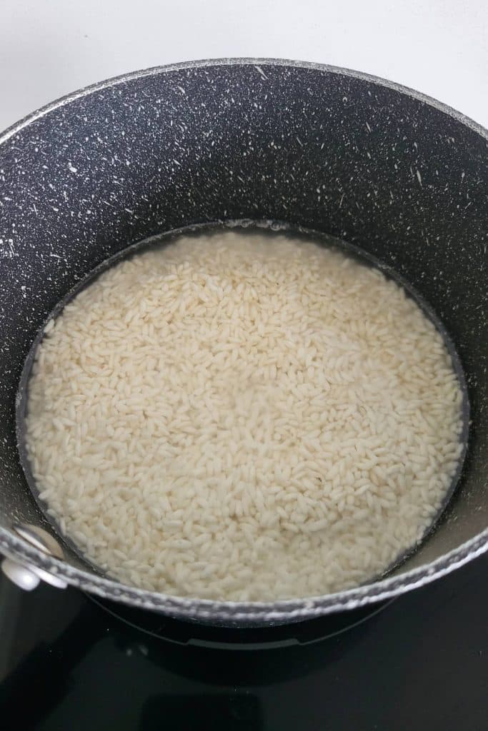 Raw sticky rice soaked in water in a saucepan.