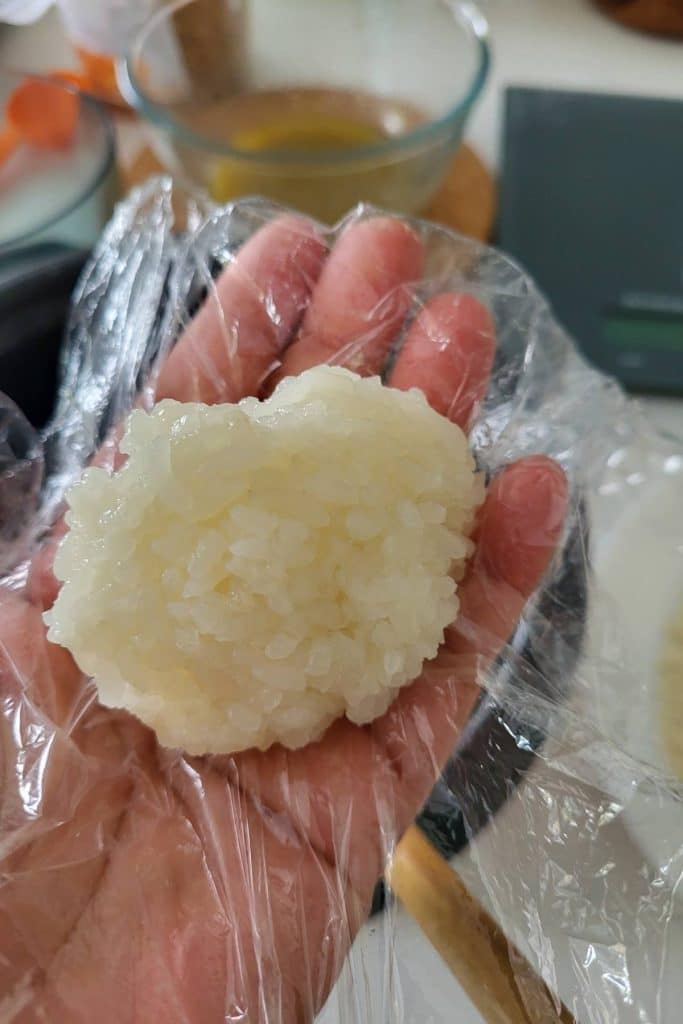 Cooked glutinous rice ball on a cling film lined hand palm.