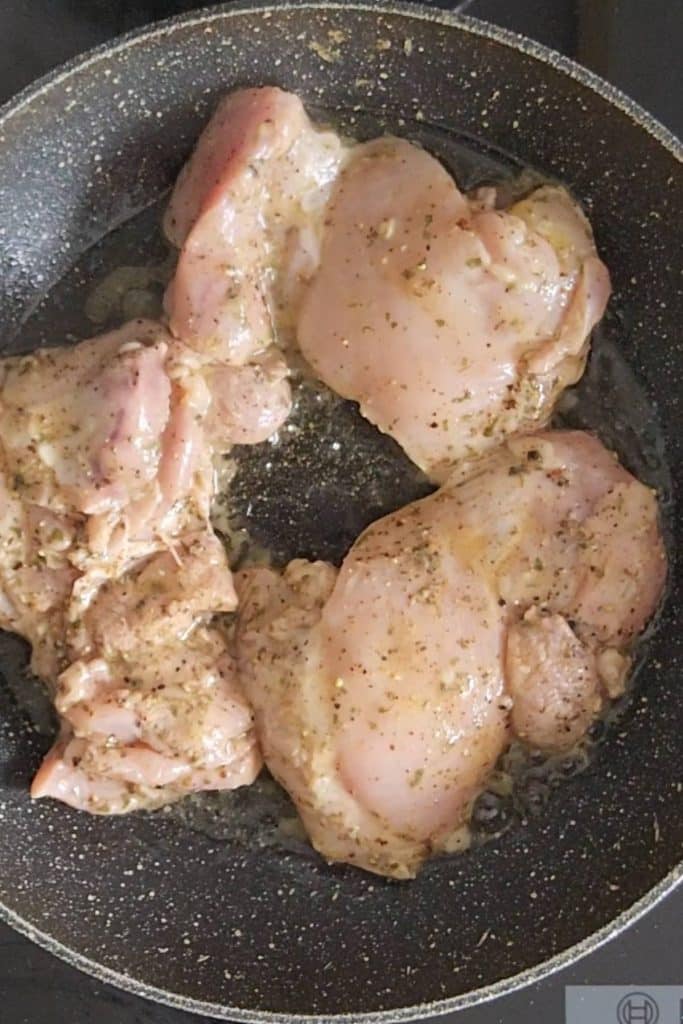 Raw chicken thighs covered with spices on a frying pan.