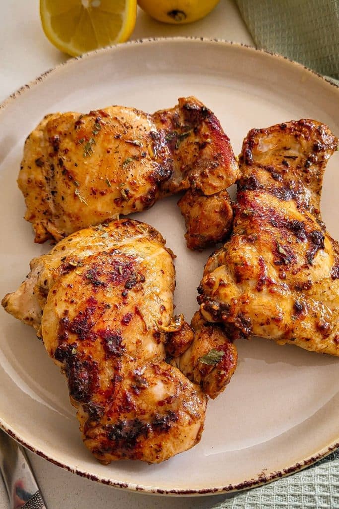Pan roasted lemon pepper chicken thighs on a round plate.