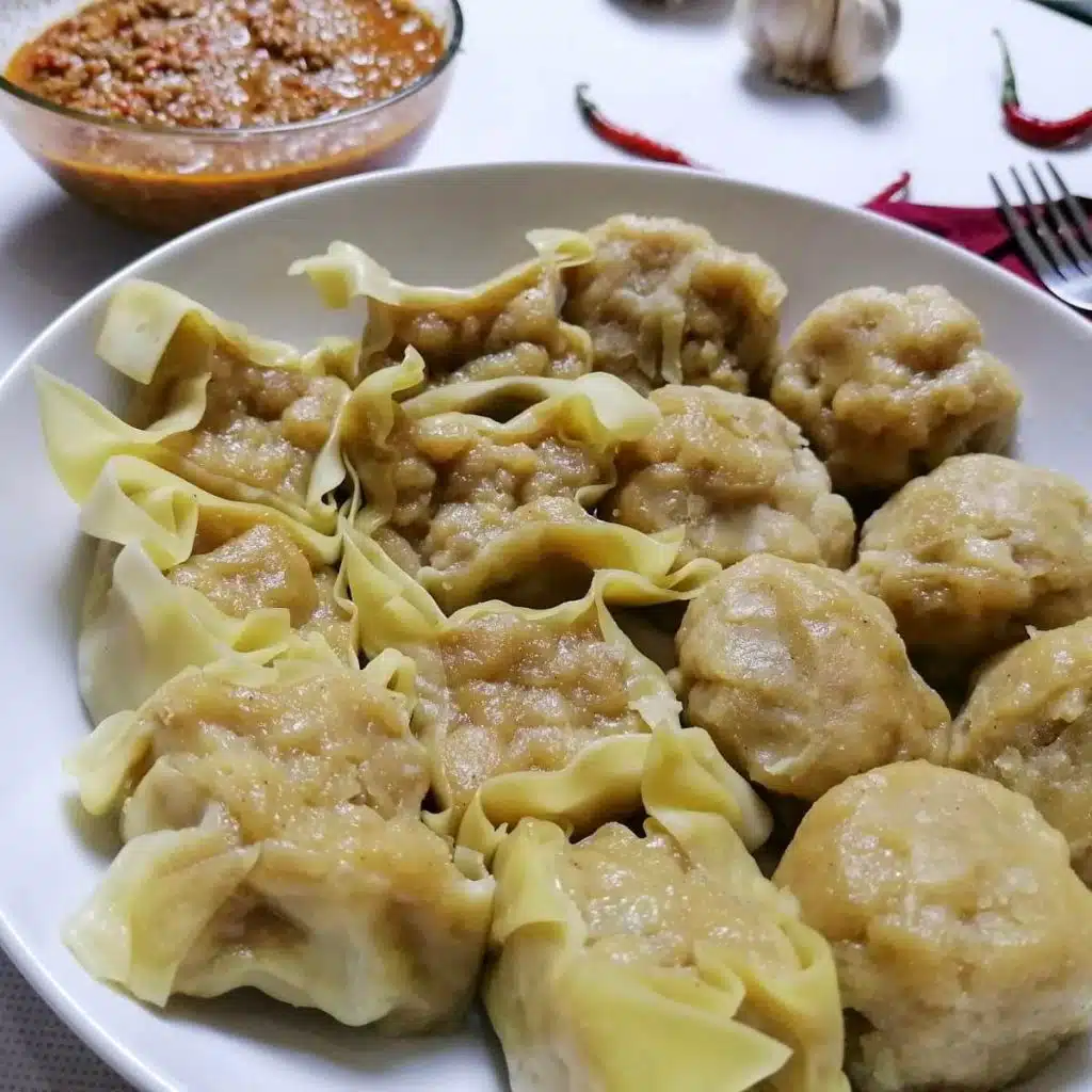 Siomay on a white plate with peanut sauce in the background.