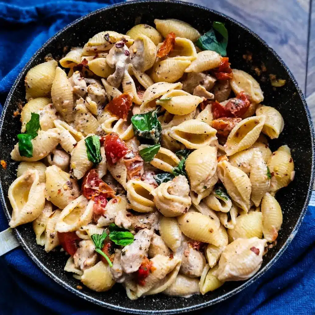 Sun-dried tomato pasta with chicken garnished with fresh basil in a skillet.