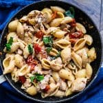 Sun-dried tomato pasta with chicken garnished with fresh basil in a skillet.