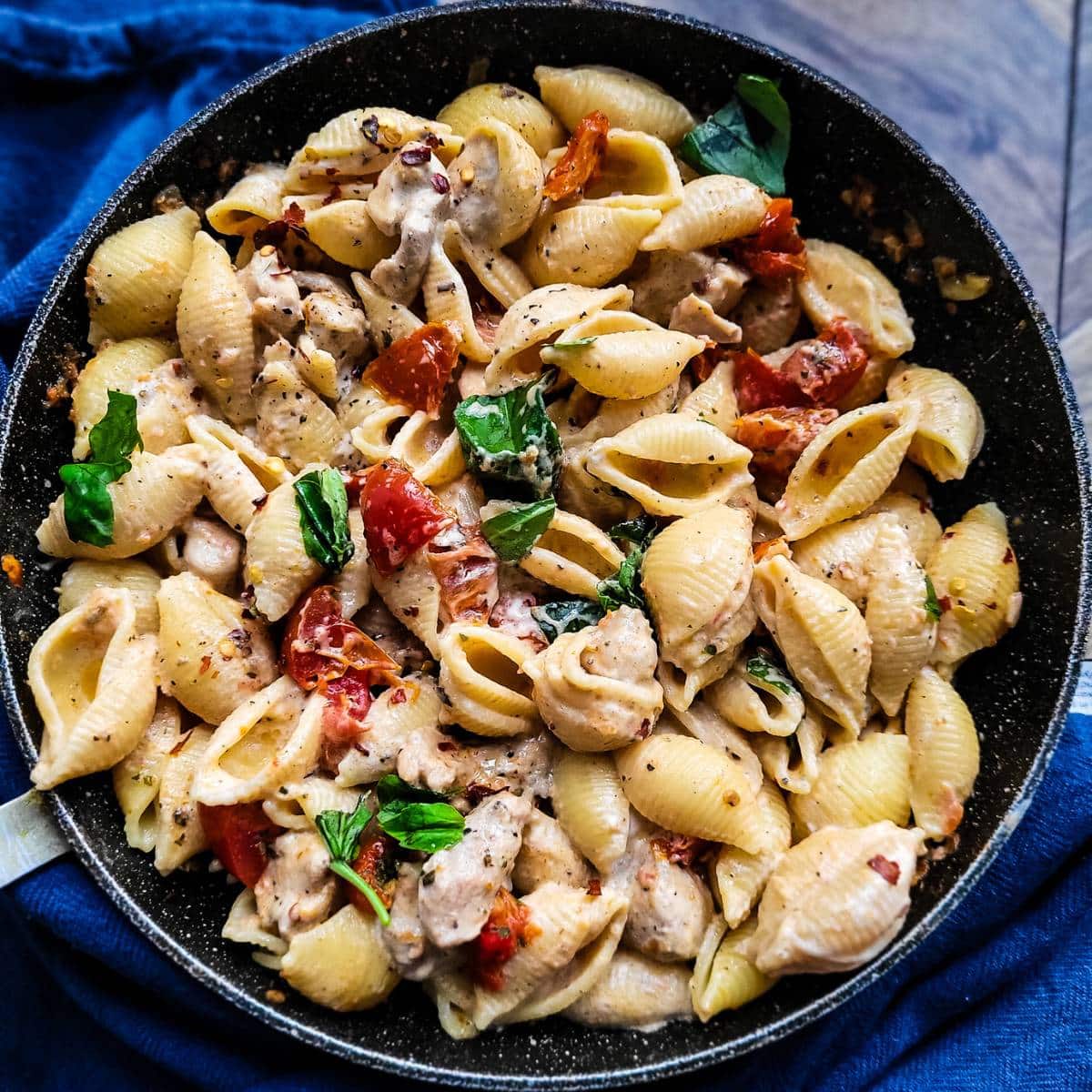Sun-dried tomato pasta with chicken garnished with fresh basil in a skillet.