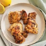 Cooked lemon pepper chicken thighs on a round plate.