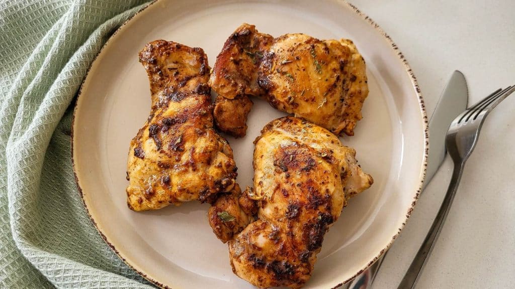 Three pieces of pan roasted chicken on a round plate with mint green napkin, fork, and knife on the background.