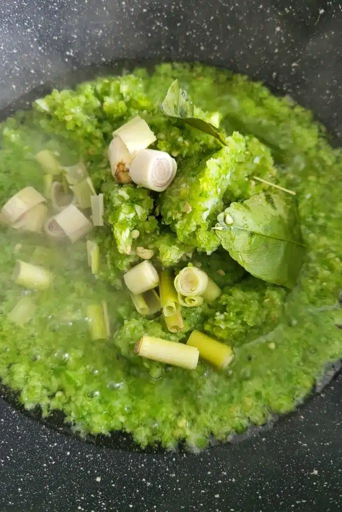 Green chilies and herbs in frying pan.