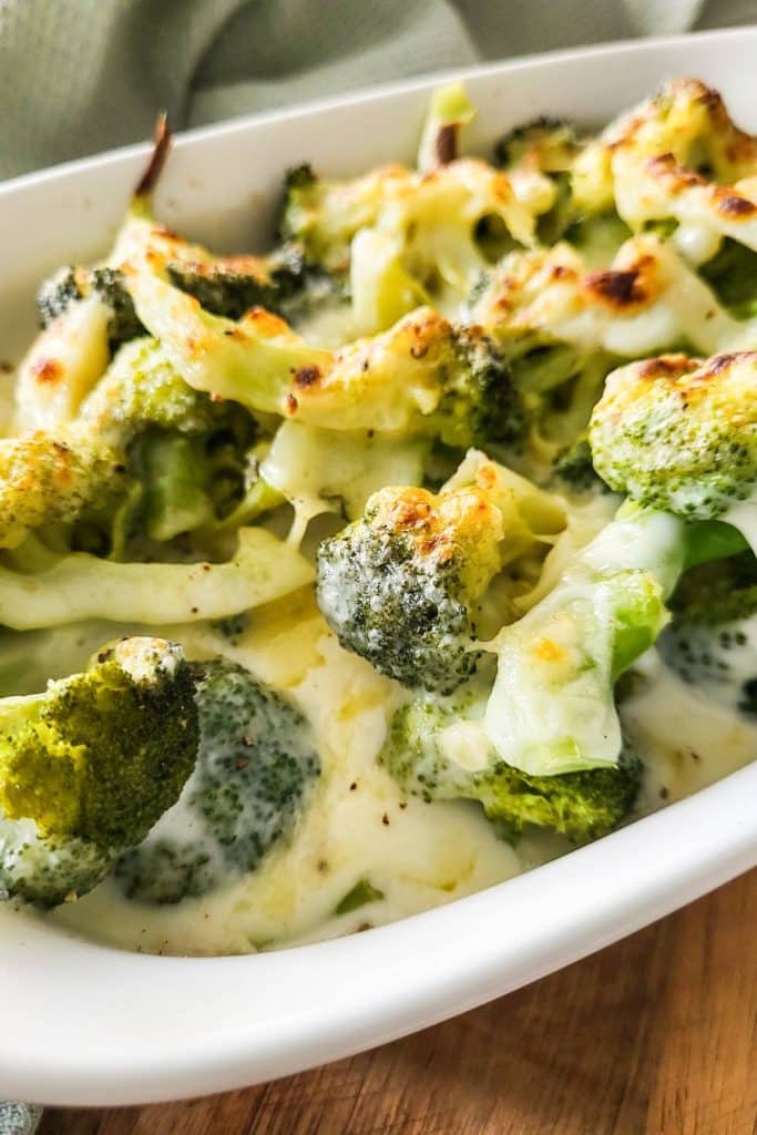 Broccoli with cheesy sauce in white casserole dish.