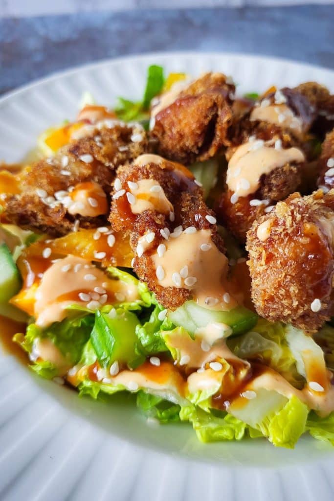 Chicken katsu pieces over lettuces and cucumbers.