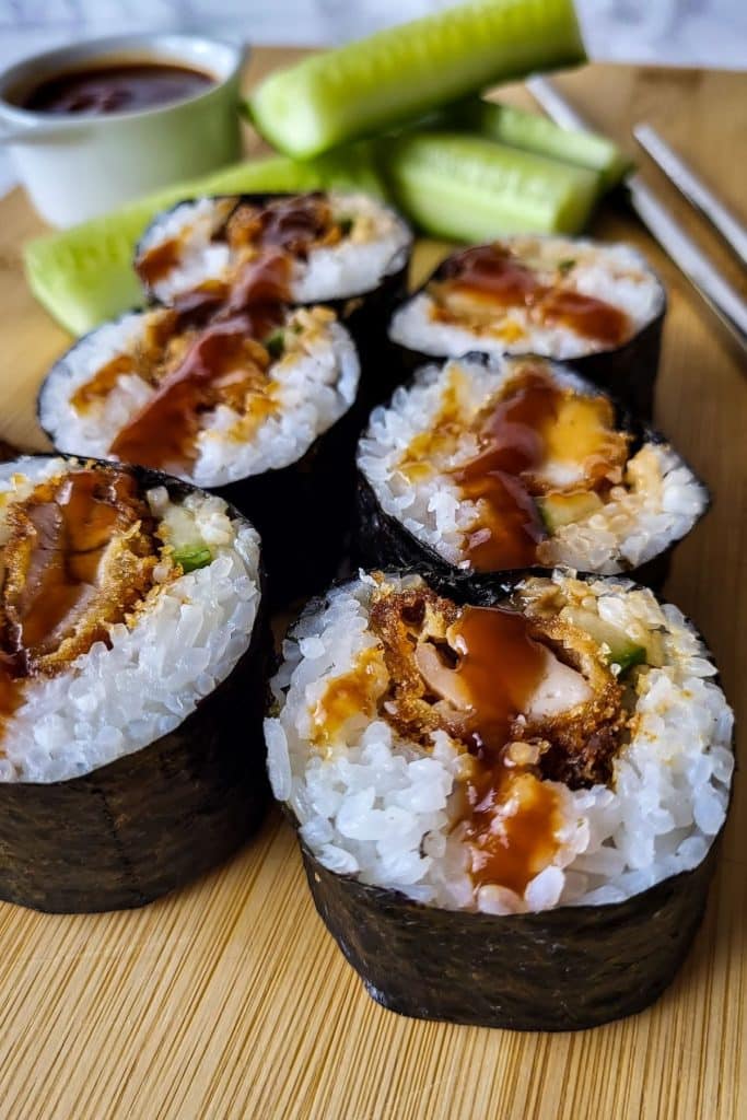 Chicken katsu sushi with cucumber, chopsticks and a small white bowl in the background.