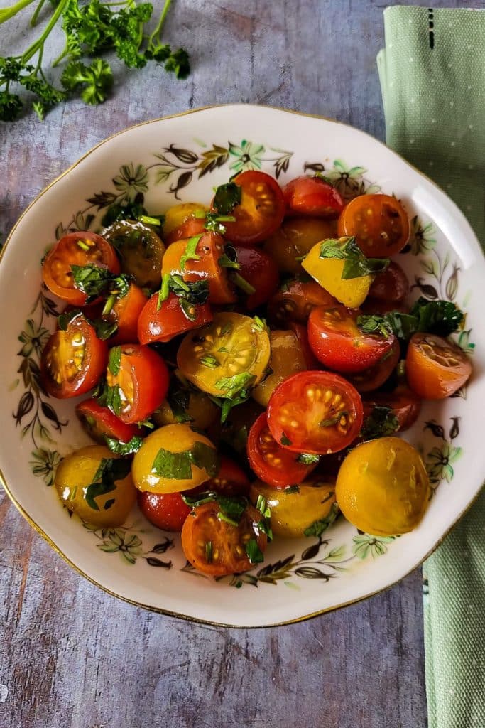 Overhead view of Italian tomato salad with halved tomatoes, parsley and black pepper in a bowl.
