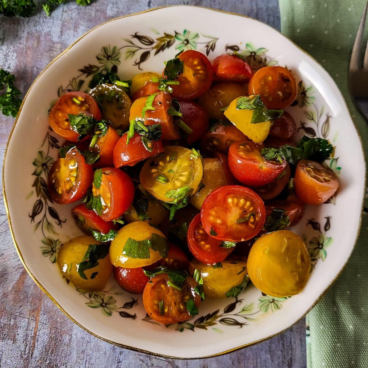 Italian tomato salad in a white bowl with fresh parsley leaves and a drizzle of olive oil.