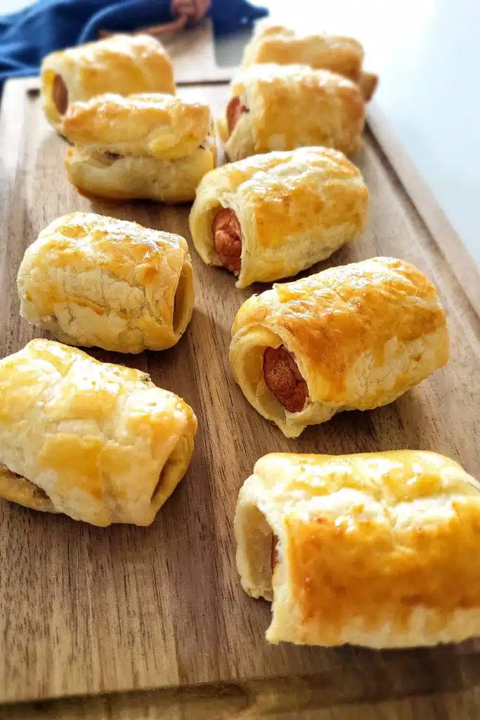 Puff pastry sausage rolls on a wooden chopping board.