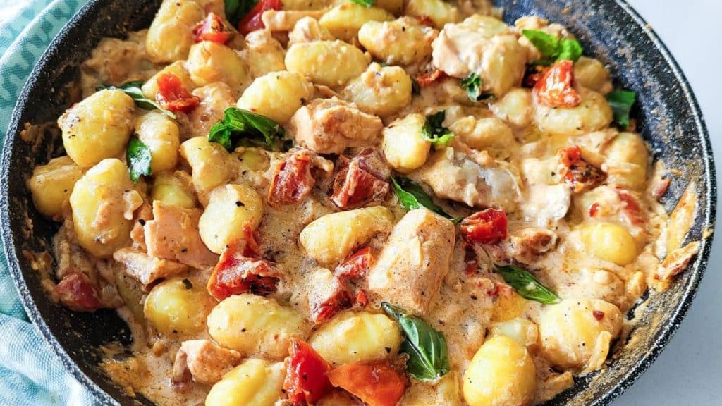 Salmon gnocchi with sundried tomatoes and fresh basil in a skillet.