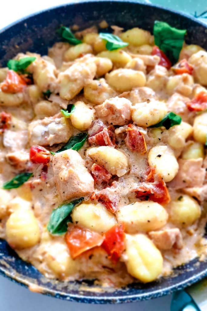 A close-up creamy gnocchi with salmon, sundried tomatoes and fresh basil.