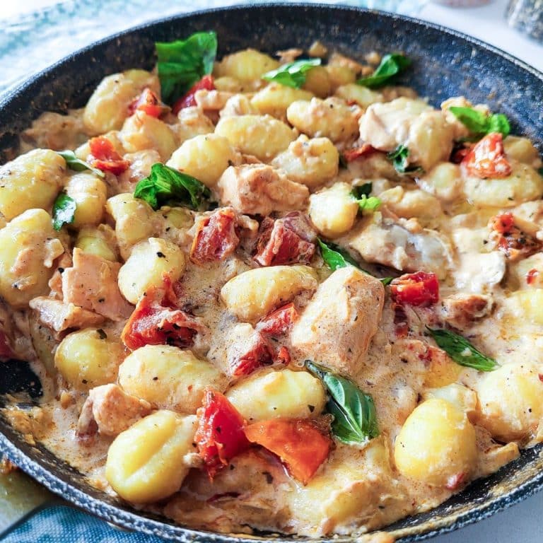 Creamy salmon gnocchi with sundried tomatoes, fresh basil in a frying pan.