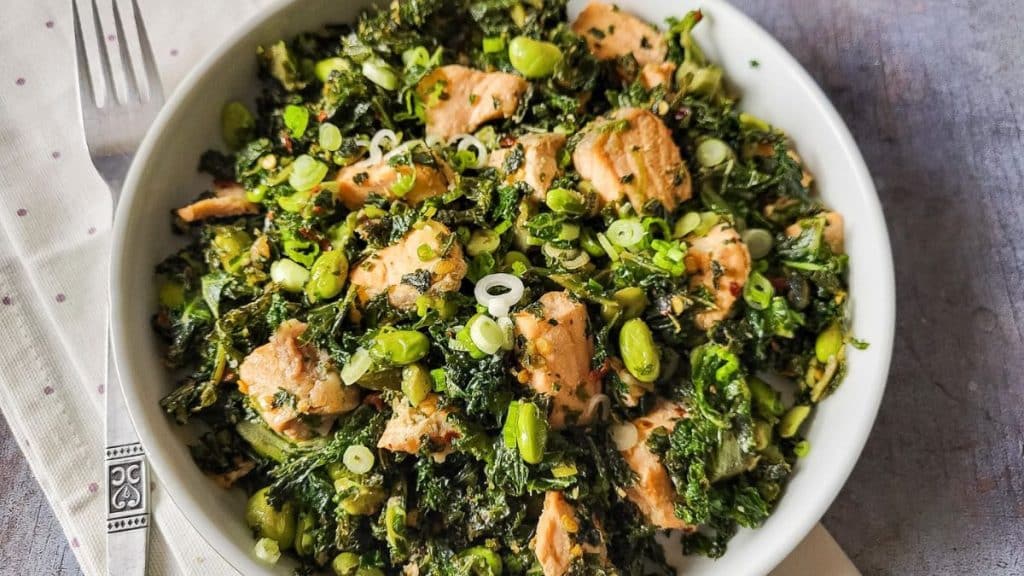 Salmon and Kale Salad in a white bowl with polka dot napkin and a fork in the background.