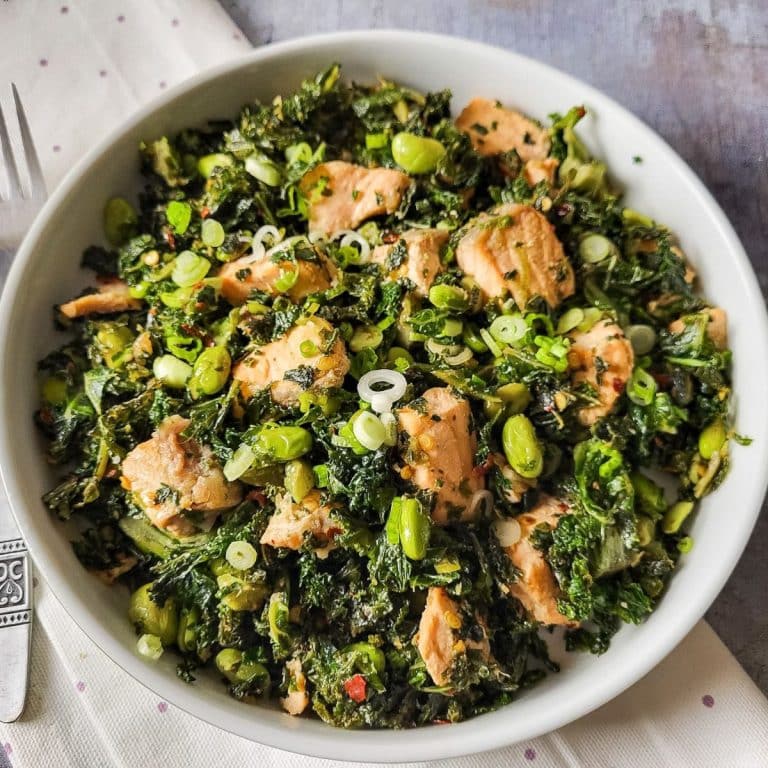 Salmon kale salad with edamame beans and spring onions in a white pasta bowl.
