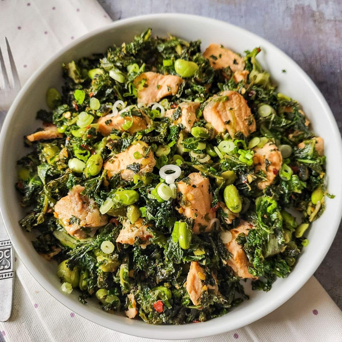 Salmon kale salad with edamame beans and spring onions in a white pasta bowl.