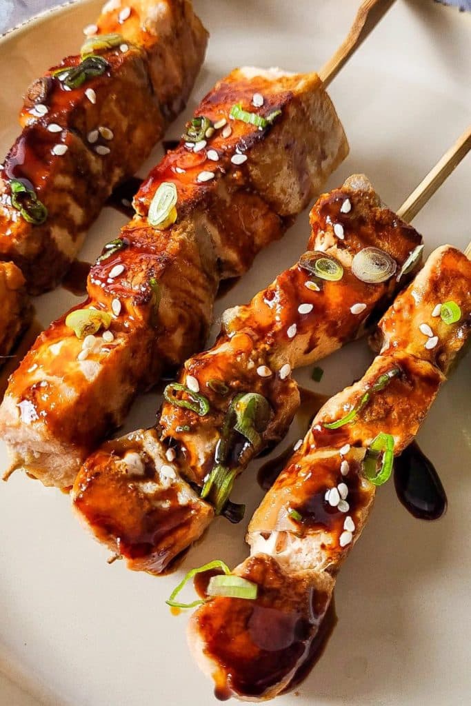Close-up Salmon Teriyaki on skewers garnished with sliced spring onion and sesame seeds.