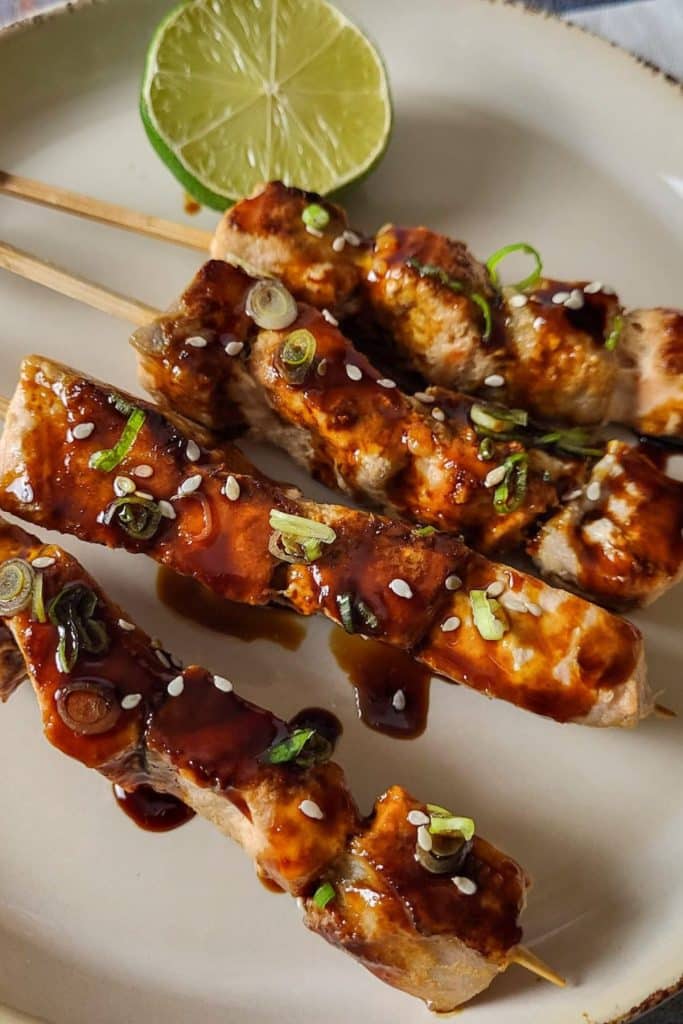 4 skewers of salmon yakitori covered with teriyaki sauce and garnished with spring onions and sesame seeds.