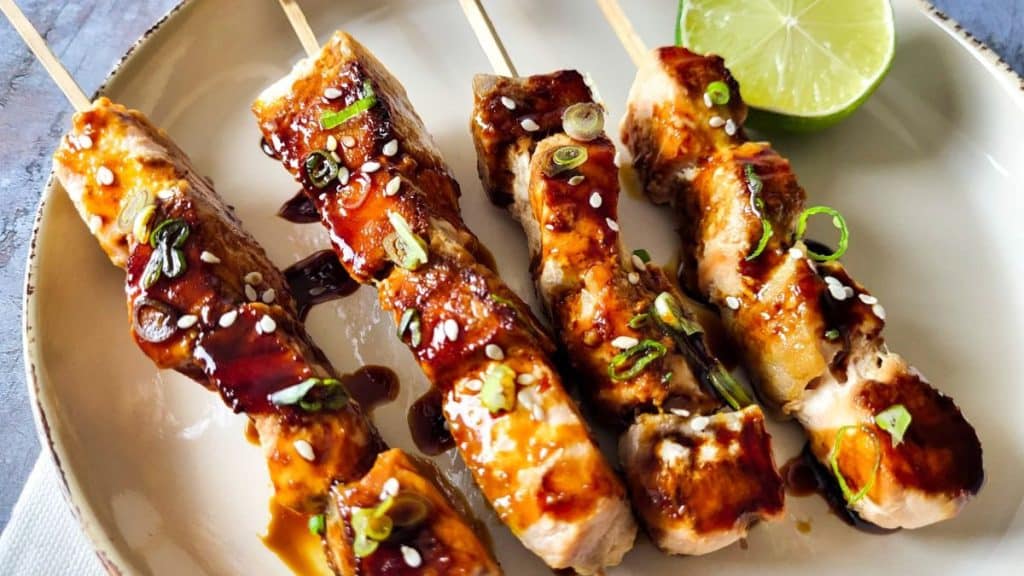 4 salmon yakitori skewers on a brown plate.