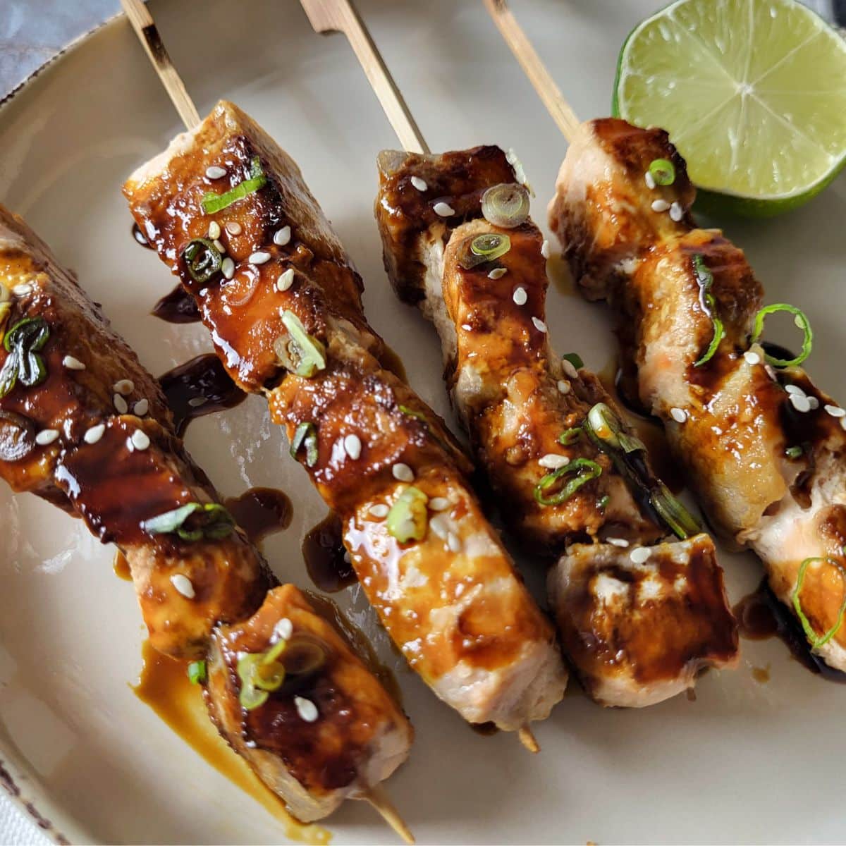 Salmon yakitori skewers with lime on a brown plate.