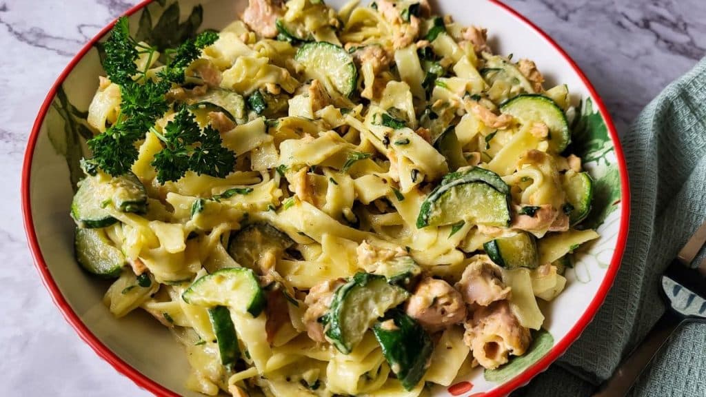 Tagliattelle pasta with salmon and zucchini in a bowl on a dining table styled as a ready-made meal.