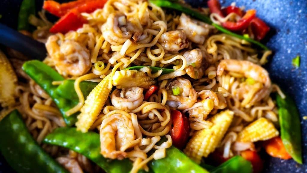 Close-up of shrimp lo mein noodles with vegetables in a frying pan.
