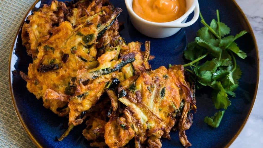 Sweet potato and zucchini fritters with a bowl of spicy mayo and parsley leaves on a blue plate.