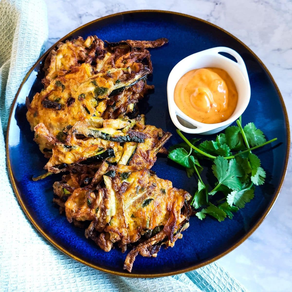 Sweet potato and zucchini fritters on a blue plate with a bowl of spicy mayo and parsley.