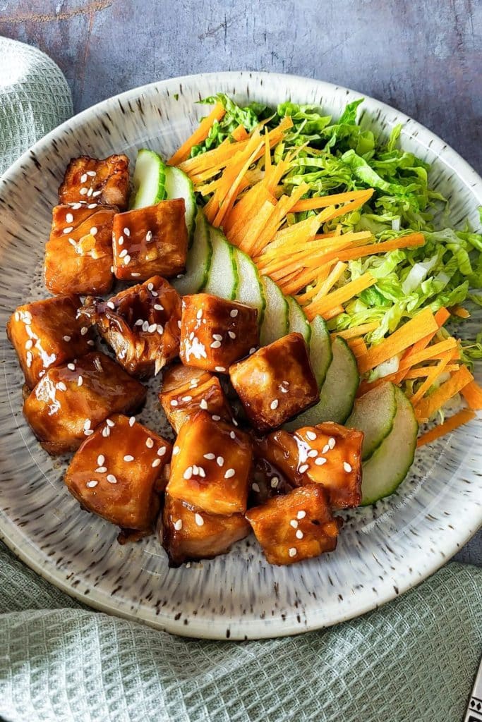 A plate of salmon bites in teriyaki sauce with sliced cucumber, carrots and lettuces.