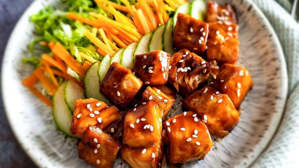 Air fried salmon bites in teriyaki sauce with cucumber, carrots and lettuces in a patterned plate.